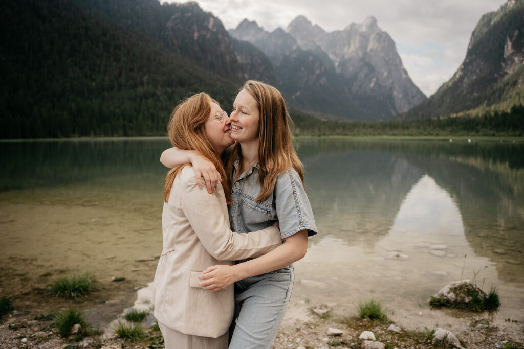Two people embrace by a scenic mountain lake.
