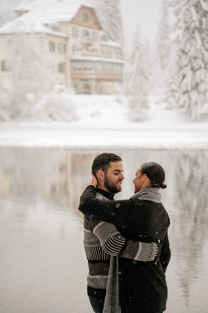 Couple embracing by snowy lake, wintery backdrop.