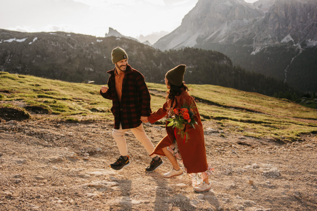 Couple hiking in mountains, holding hands, bouquet in hand.
