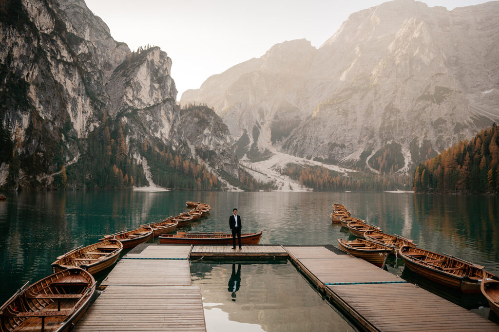 Man standing on dock with mountain lake backdrop.