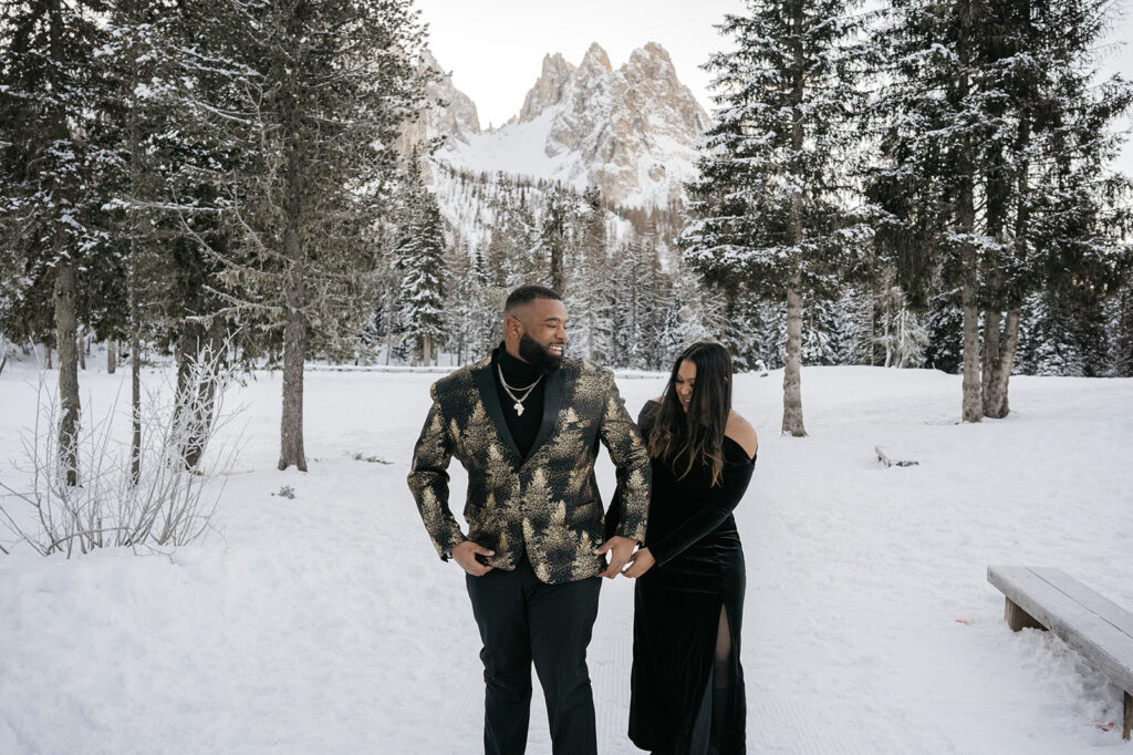 Couple walking in snowy forest with mountains.