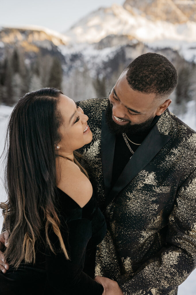 Smiling couple embracing in snowy mountain landscape.