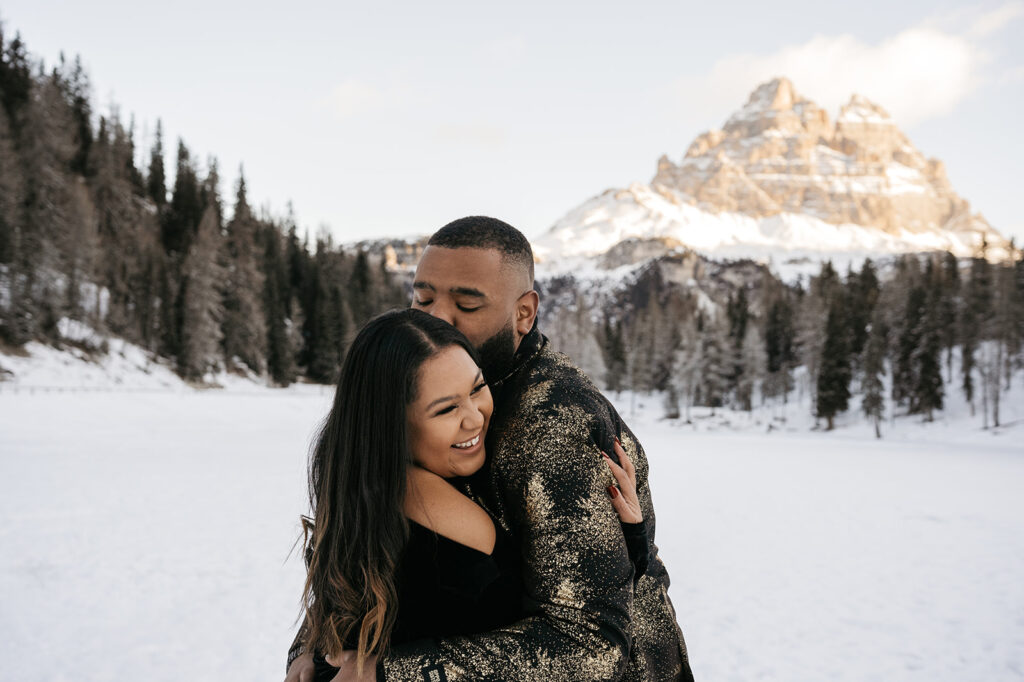 Couple embraces in snowy mountain landscape.