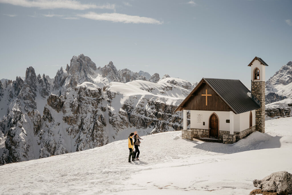 Snowy mountain chapel with hikers in winter landscape.