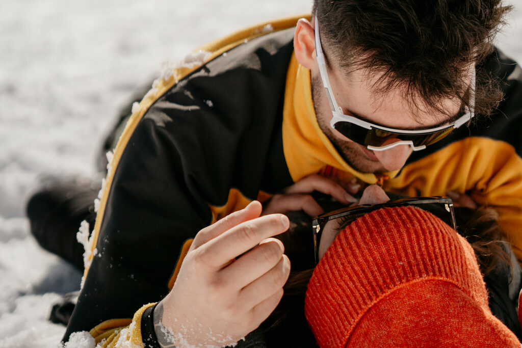 Couple embracing in snow wearing sunglasses and hats.