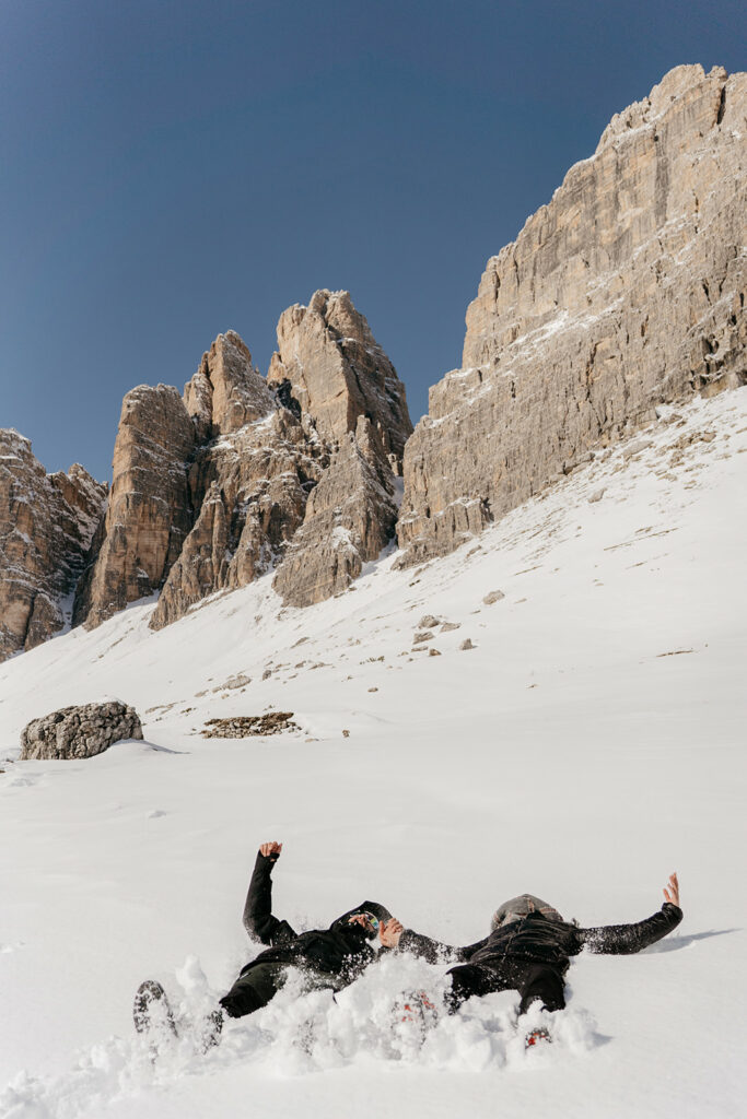 People playing in snow beneath rocky mountains.