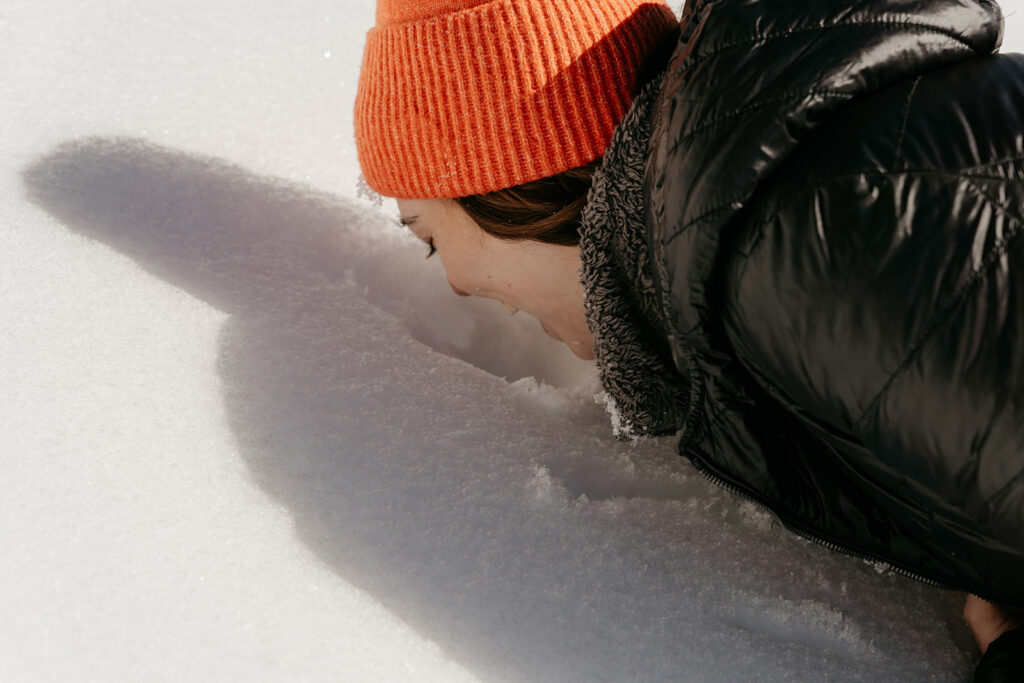 Person smelling snow while wearing orange beanie.