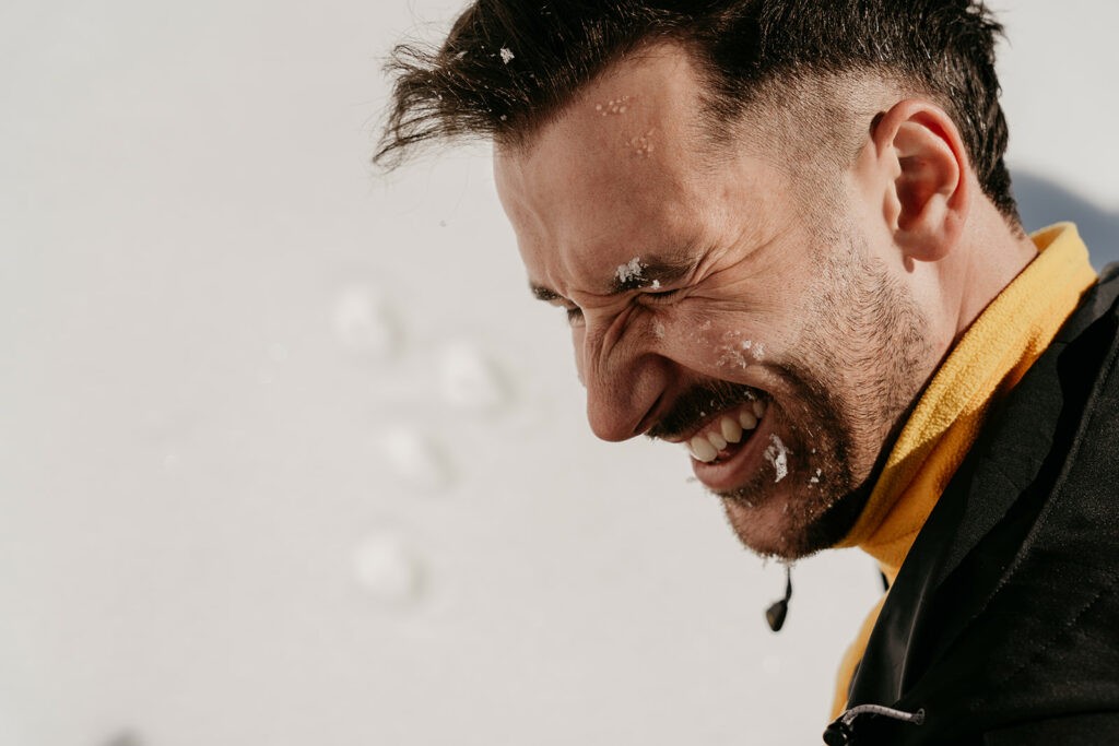 Laughing man with snow on face in sun.