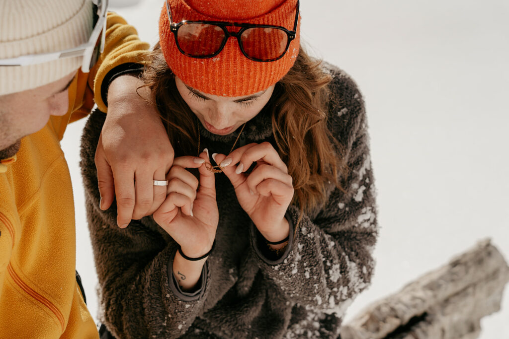 Couple admiring jewelry in snowy landscape.