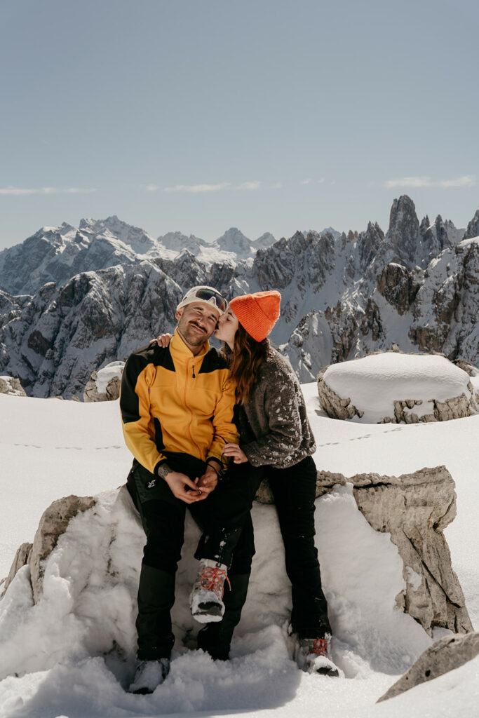 Couple embracing on snowy mountain with scenic view.