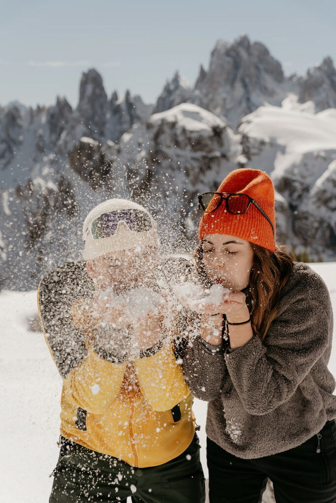 Two people blowing snow in snowy mountains.