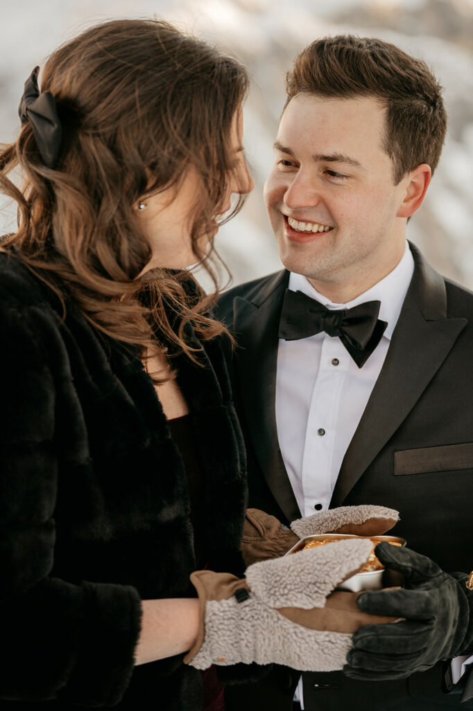 Couple smiling, wearing formal attire in snowy setting.