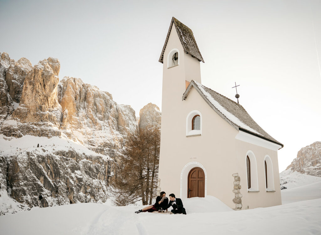 Snowy mountain chapel with people sitting outside