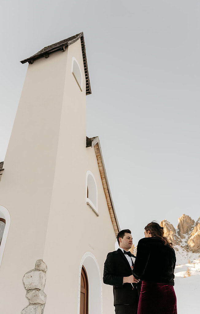 Couple holding hands near mountain chapel.