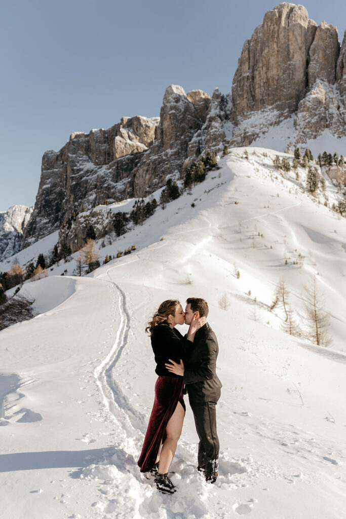 Couple kissing on snowy mountain path.