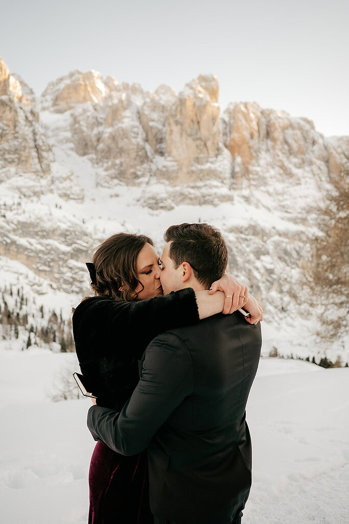 Couple kissing in snowy mountain landscape.