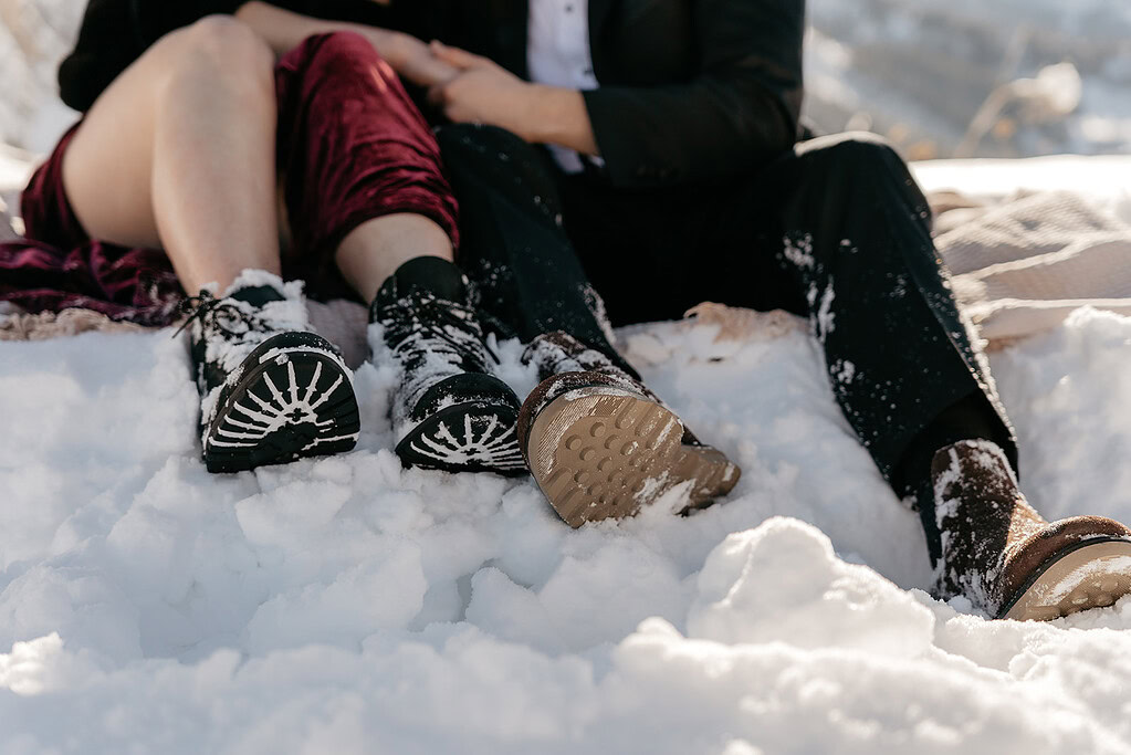 Couple sitting in snow with snowy boots.