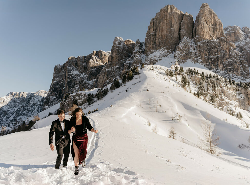 Couple in formalwear climbing snowy mountain.