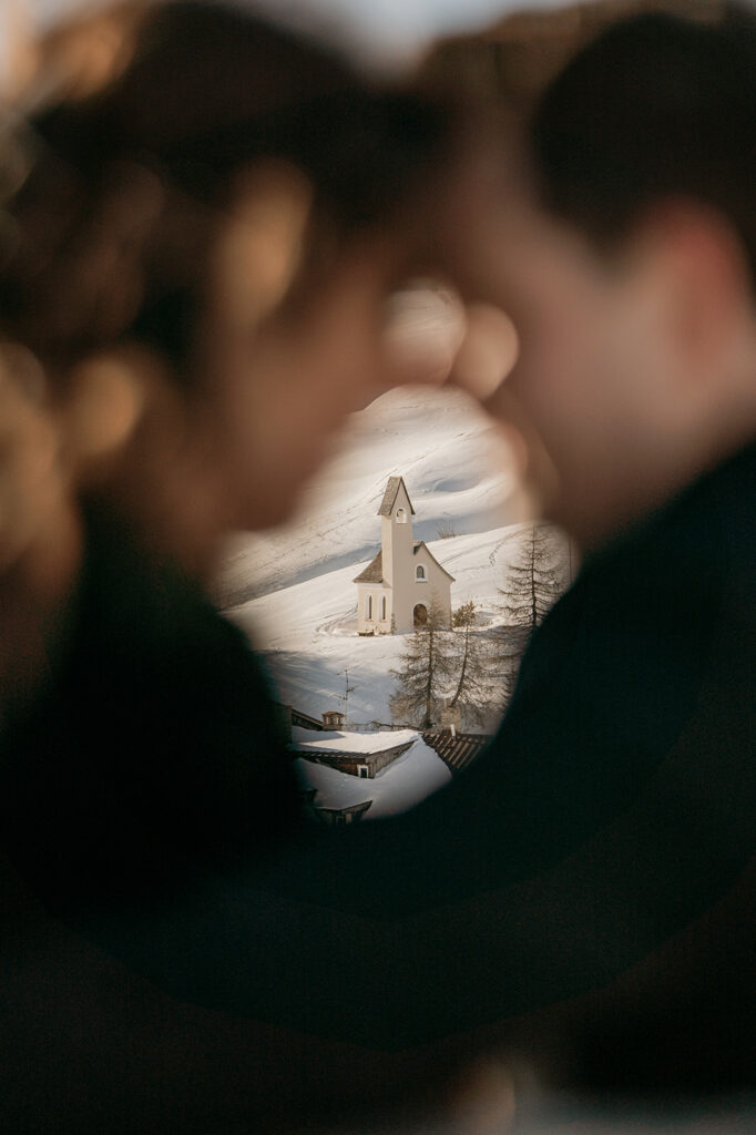 Distant snow-covered chapel framed by blurred figures.