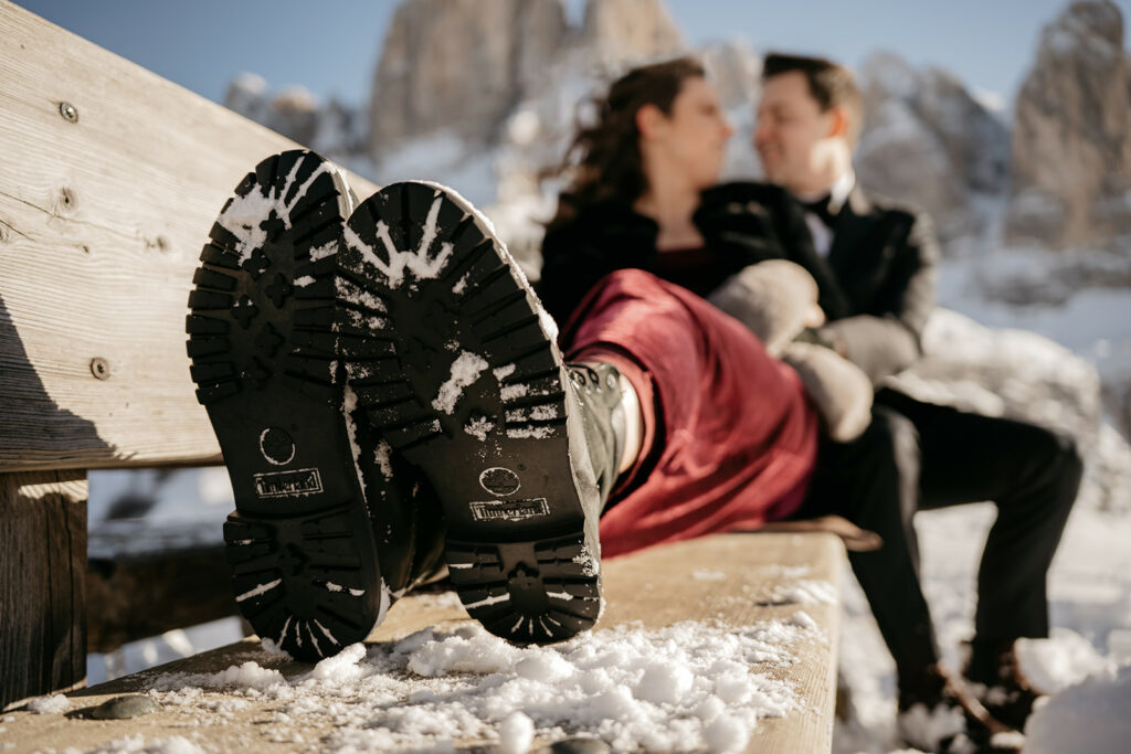 Couple embracing on snowy bench, boots in focus.