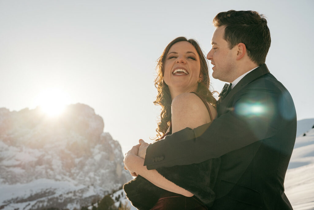 Smiling couple embraces in snowy mountain landscape.