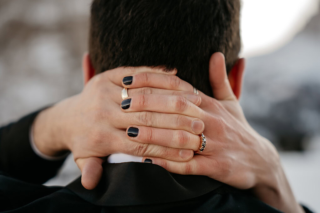 Hands with black nails on head, wearing rings.
