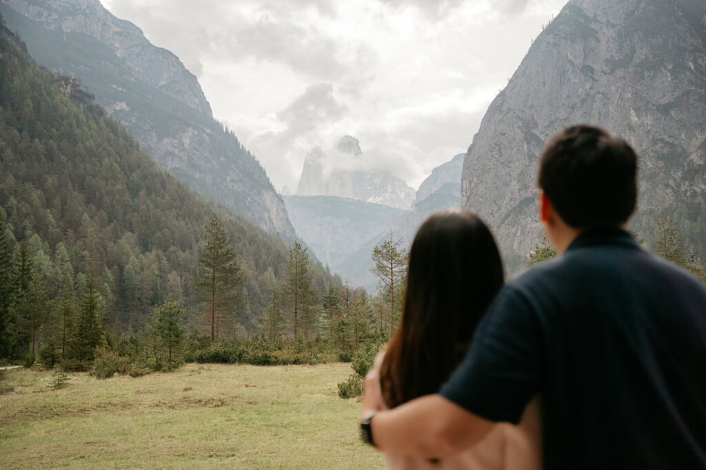 Couple embraces, views scenic mountain landscape.