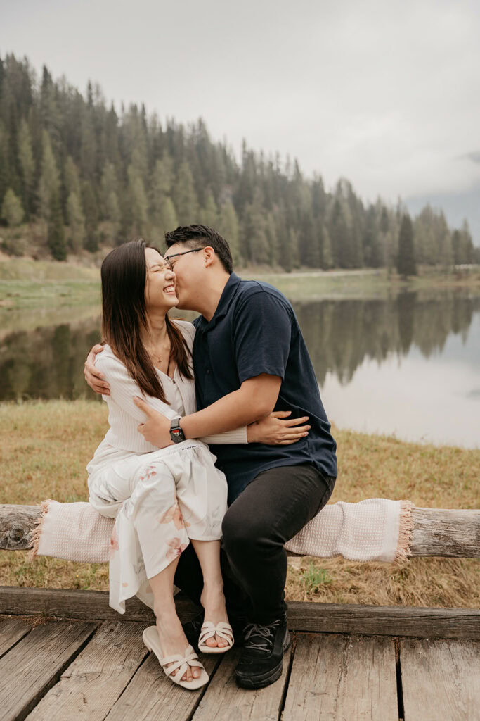 Couple laughing near a serene forest lake.