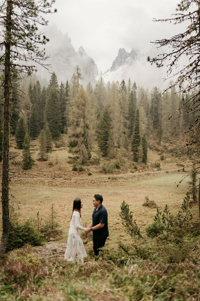 Couple holding hands in misty forest.