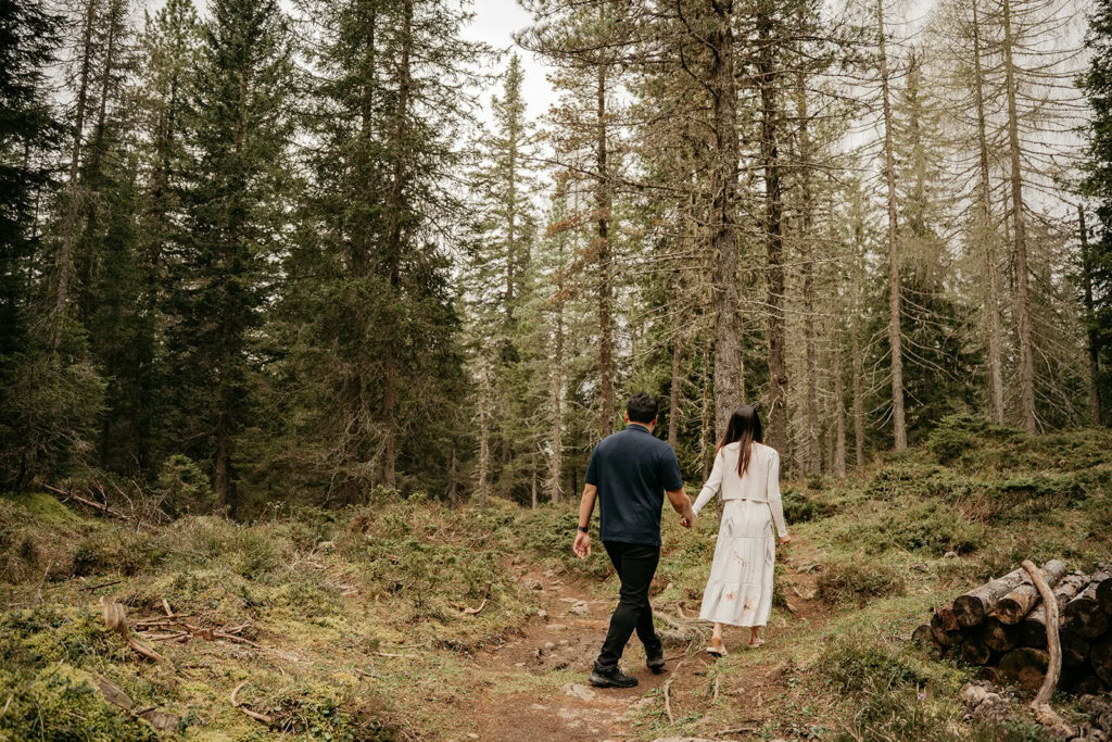 Couple walking hand in hand through forest.