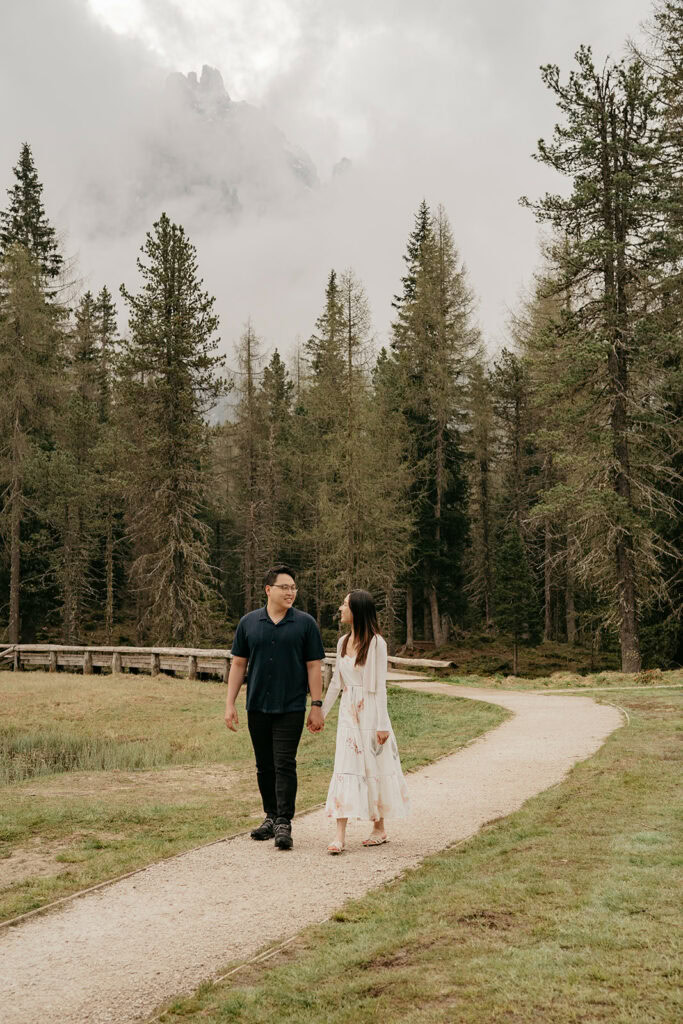 Couple walking on forest path, misty mountains behind.