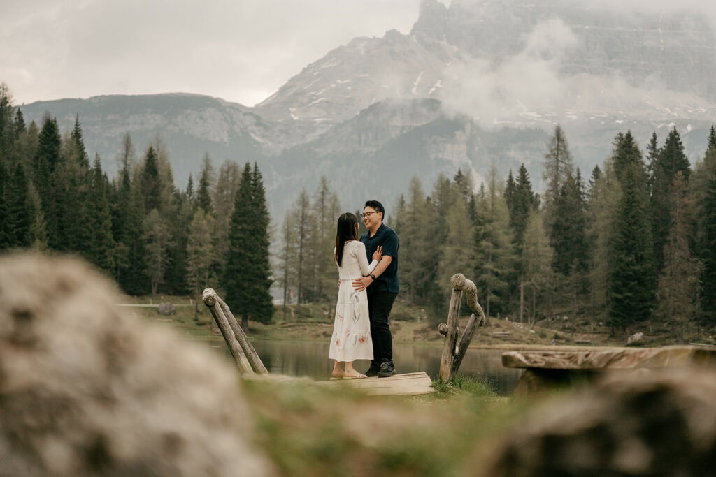 Couple embraces on wooden bridge in forest setting.
