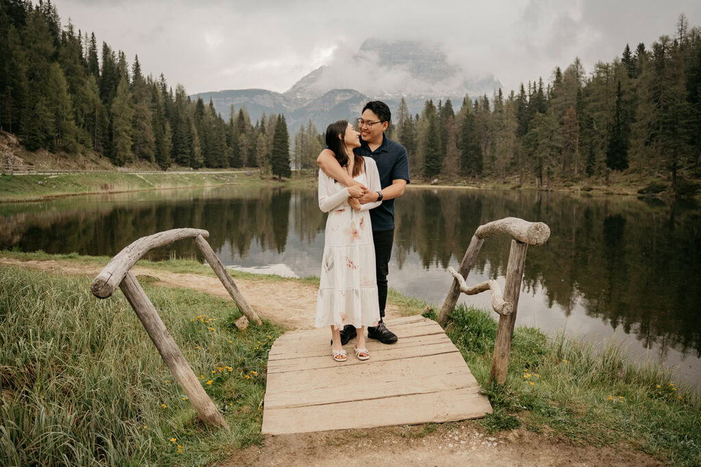 Couple embracing on bridge by scenic lake view.