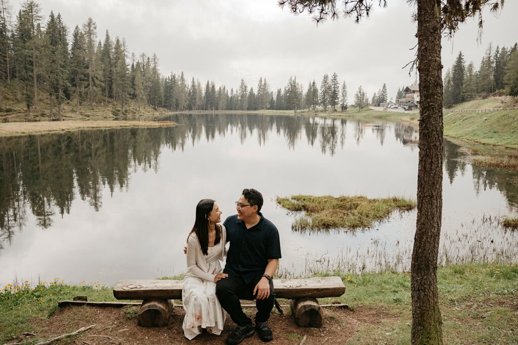 Couple sitting on bench by tranquil lake.