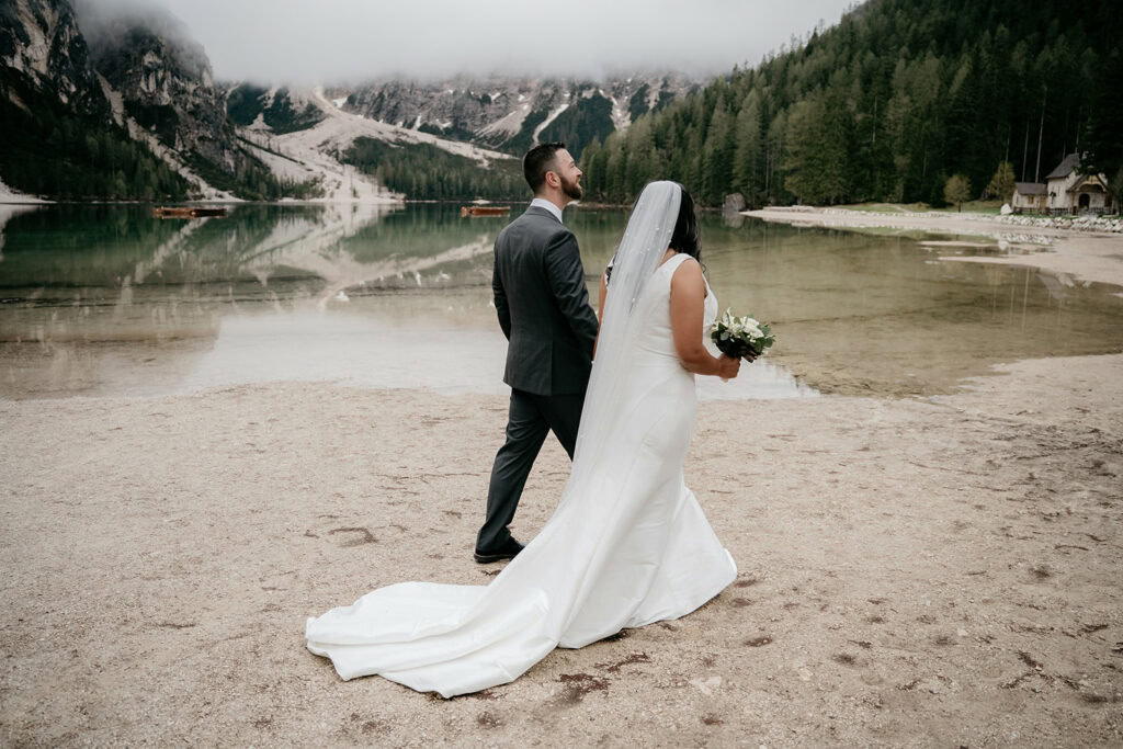 Bride and groom by scenic lake, mountain backdrop.