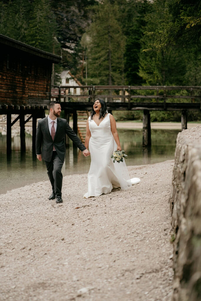 Bride and groom laughing by a lakeside cabin.