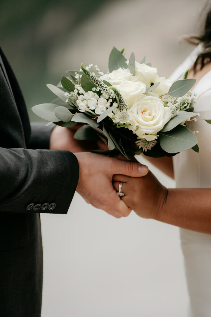 Couple exchanging vows, holding white flower bouquet.