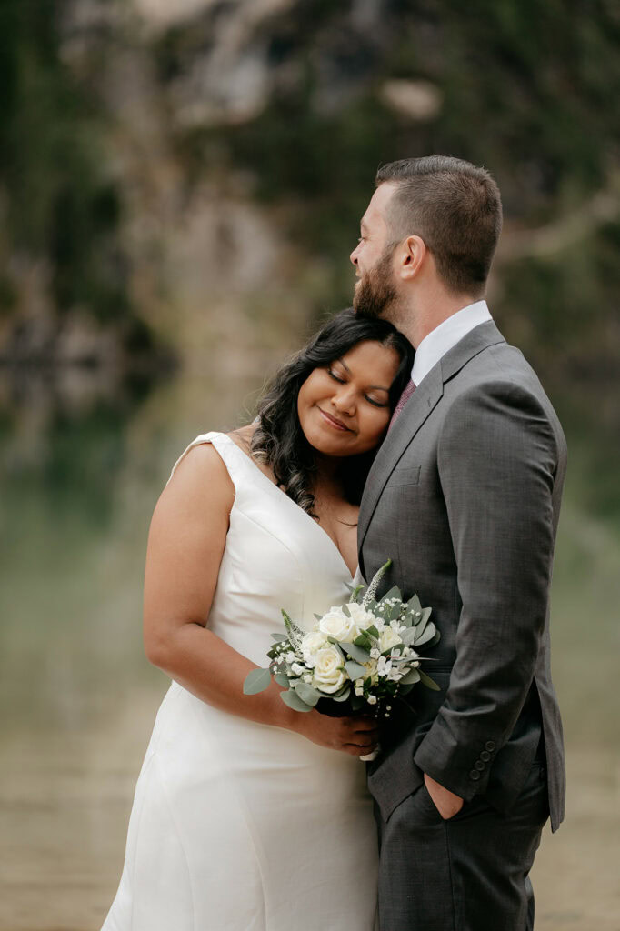 Bride and groom embracing by lakeside.