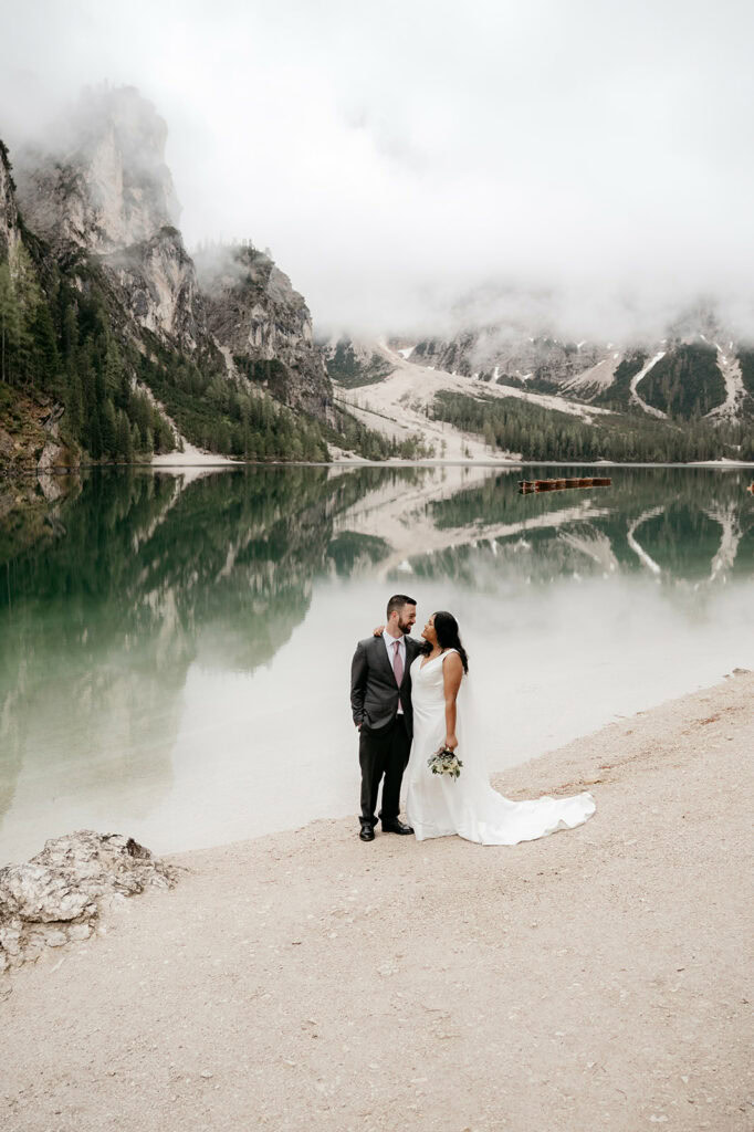 Couple posing by misty mountain lake on wedding day.