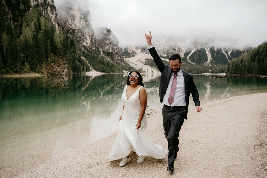 Happy couple celebrates beside a serene mountain lake.
