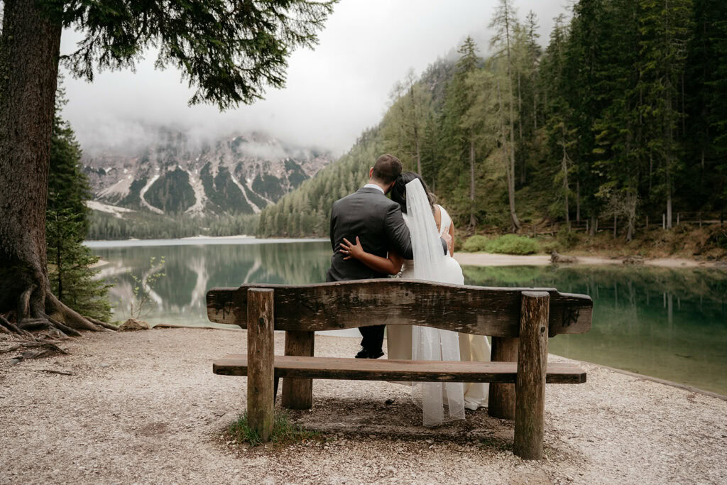 Couple on a lakeside bench, misty mountains behind.