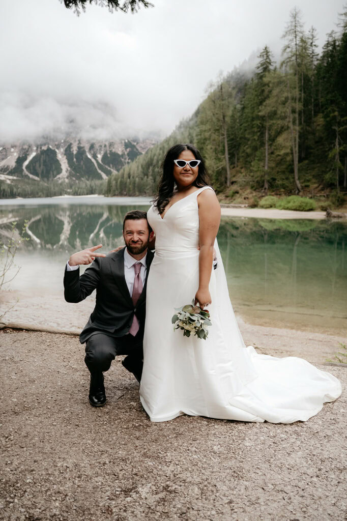 Couple poses by lake in wedding attire.
