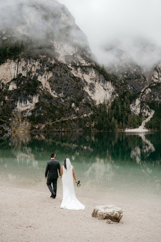 Bride and groom walk by mountain lake