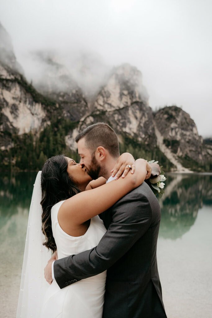 Bride and groom kissing by a mountain lake.