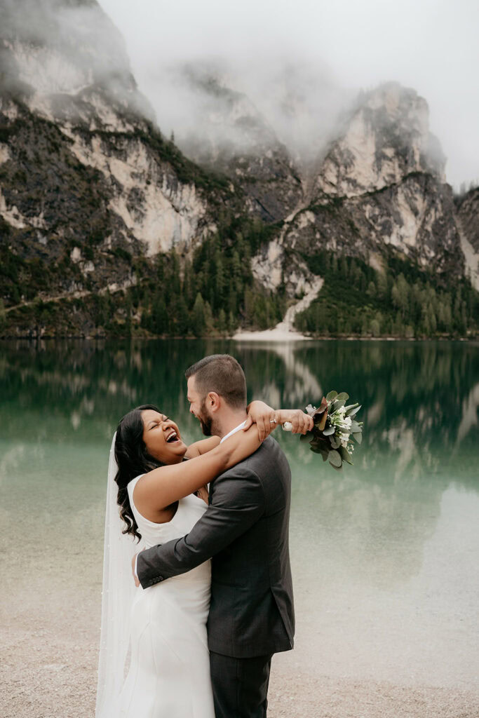 Bride and groom hugging by a mountain lake.
