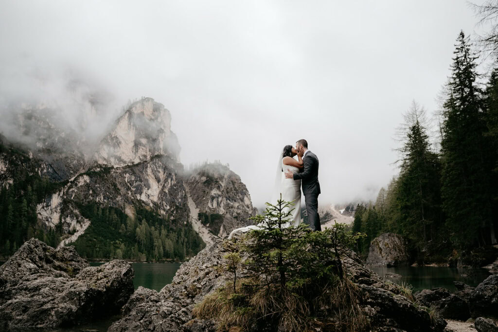 Couple kissing on mountain cliff, surrounded by mist.