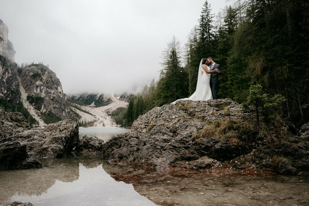 Bride and groom embrace on rocky mountain overlook.