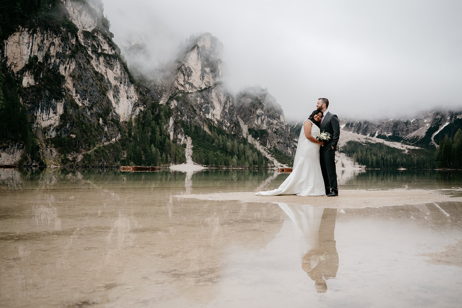 Bride and groom by a serene mountain lake.