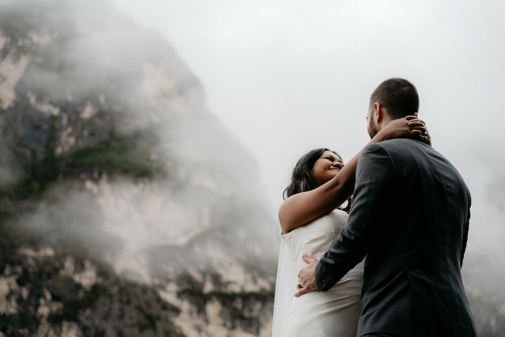 Couple embraces in front of misty mountain landscape.