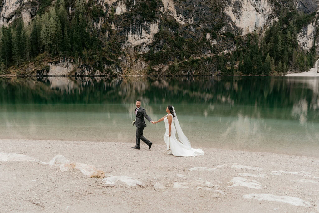 Bride and groom walking by mountain lake.